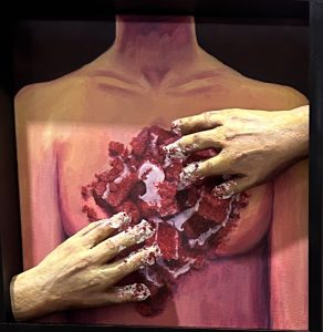 A painted torso with two hands gripping a heart made of red velvet cake, creating a surreal and striking visual.