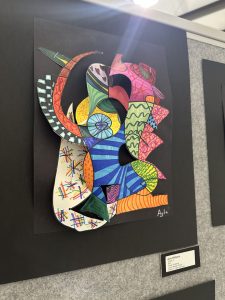 Colorful abstract sculpture featuring various shapes and patterns, displayed on a black background at an art exhibit.