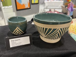 Two ceramic bowls are displayed on a black cloth, featuring geometric designs and a teal glaze. A label provides details.