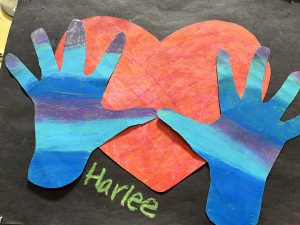 Colorful handprints in blue and purple surround a red heart, with the name "Harlee" written in green below.