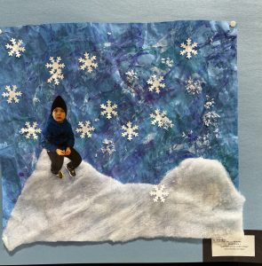 Un niño está sentado en una colina nevada sobre un fondo azul con copos de nieve blancos, en un collage de temática invernal.