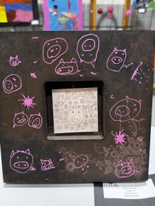 A decorative frame with pink pig illustrations surrounding a central drawing of various pig faces.