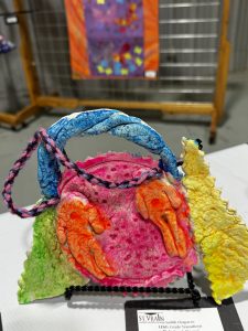 Colorful paper craft shaped like a purse, featuring bright hands and a decorative handle, displayed on a stand.