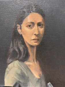 A portrait of a woman with long dark hair, wearing a green top, against a dark background, looking directly at the viewer.