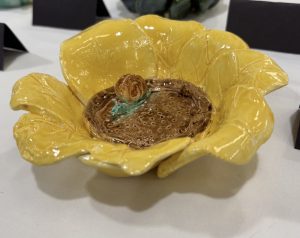 A ceramic dish shaped like a yellow flower, featuring a brown center and a small green accent.