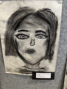 A charcoal portrait of a woman with striking eyes and dark hair, mounted on a display board.