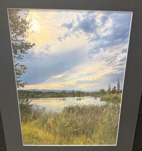 A serene landscape featuring a calm lake, lush greenery, and a cloudy sky with soft sunlight breaking through.