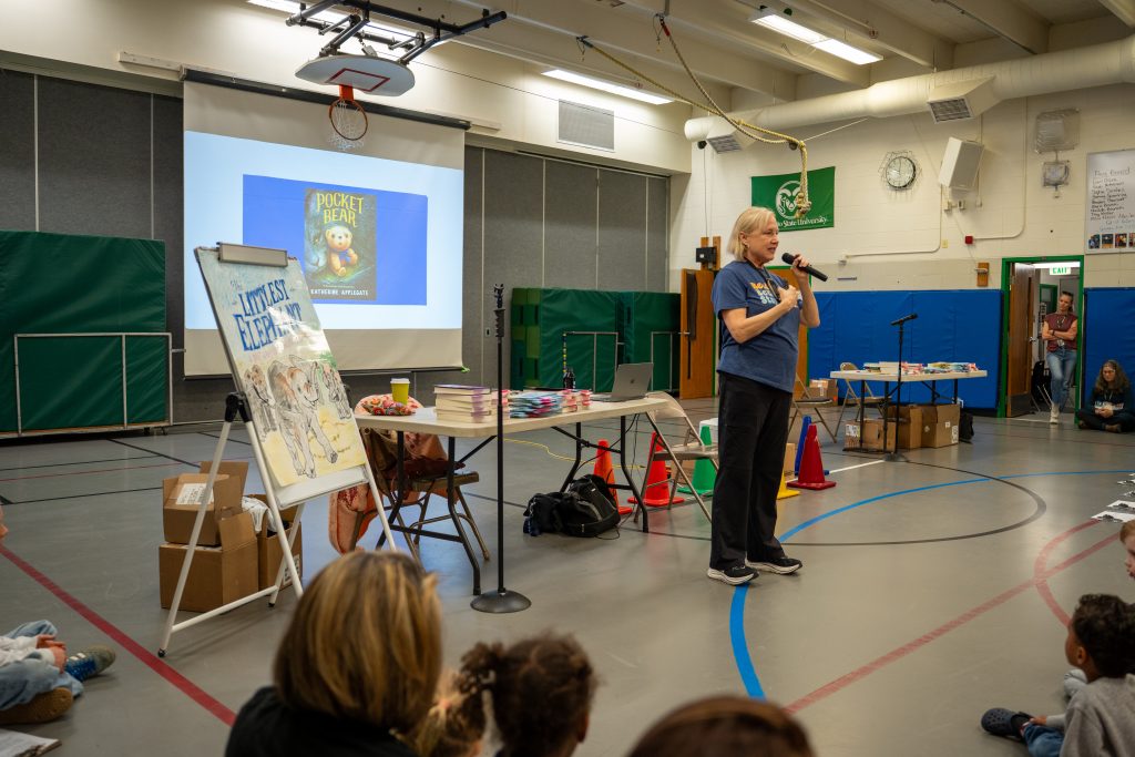 Katherine Applegate speaks to children at Niwot Elementary, with books and a projector screen displaying "Pocket Bear."