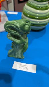 A green sculpture displayed on a blue table, labeled with the artist's name and school information.