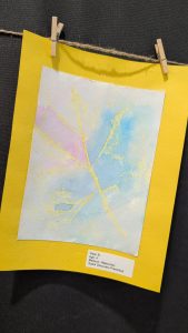 A watercolor painting by a four-year-old, featuring soft colors and leaf-like patterns, displayed on yellow paper.