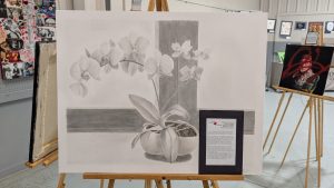 Black and white drawing of an orchid in a pot, displayed on an easel at an art exhibit.