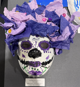 Colorful paper mache skull with purple and pink tissue paper hair, decorated with beads and painted details.