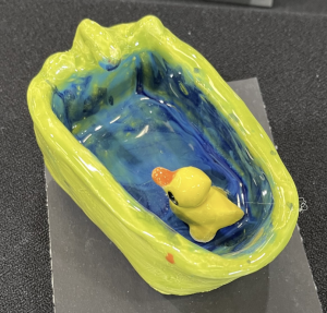 A small, colorful ceramic dish in the shape of a bathtub with a rubber duck inside.