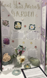 A display board titled "Knot Your Average Garden" featuring crocheted flowers, plant descriptions, and decorative elements.