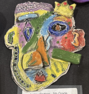 Colorful ceramic artwork shaped like a face, featuring various geometric designs and textures. Created by a 5th grader.