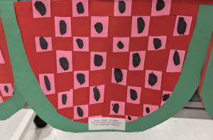 Colorful paper art depicting a watermelon with red and pink squares, featuring black seeds and a green border.