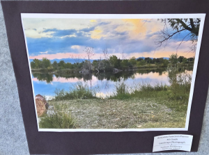A serene landscape featuring a calm lake, lush greenery, and colorful clouds at sunset.