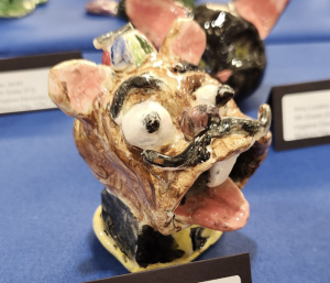 Ceramic sculpture of a cartoonish dog head with exaggerated features, colorful details, and a playful expression.