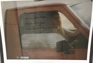 A young woman sits in a red truck, with lyrics overlayed about letting one's light shine.