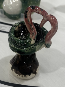 Ceramic piece featuring a black base with green and pink swan-like handles, showcasing intricate detailing.