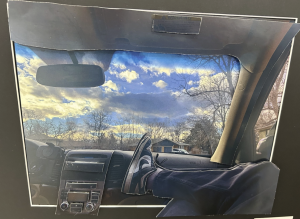 A view from inside a car showing a foot resting on the dashboard, with a scenic sky and trees visible outside.