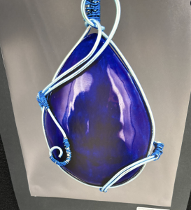 A teardrop-shaped pendant in deep blue, wrapped with light blue wire for an artistic design.