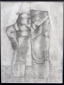 A detailed pencil drawing of two ballet shoes, laced and positioned on a wooden surface.