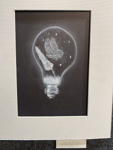A chalk drawing of a light bulb with a butterfly and stars inside, set against a dark background.