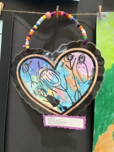 A colorful heart-shaped family portrait with drawings of four figures labeled "Mom," "Dad," and "Sister."