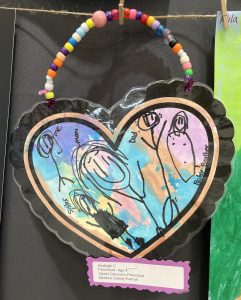 Child's colorful family portrait in a heart shape, featuring stick figures labeled as mom, dad, and sibling.