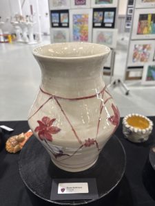 Ceramic vase with floral designs on a display table, surrounded by other art pieces in a gallery setting.