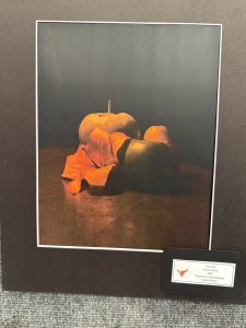 Naturaleza muerta en la que aparecen dos manzanas y una hoja roja, iluminadas con tonos cálidos sobre un fondo oscuro.