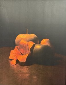 A still life featuring two apples and a wilted leaf on a dark surface, illuminated with soft lighting.