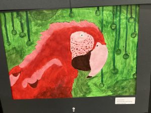 A vibrant painting of a red parrot with green foliage and hanging circles in the background.