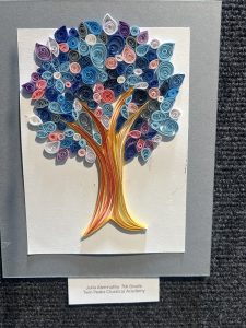 Colorful quilled tree artwork with swirling leaves in shades of blue, pink, and white, set on a light background.