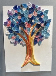 A colorful quilled tree with spirals of blue, pink, and white leaves on a textured background. The trunk is golden.