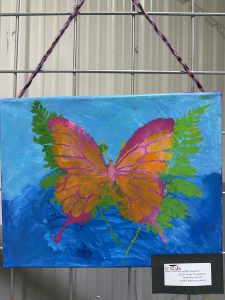 A vibrant butterfly in orange and pink hues is surrounded by green ferns on a blue background.