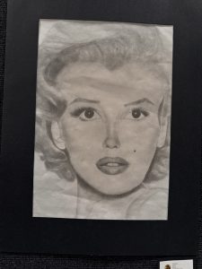 A pencil drawing of a woman with wavy hair, large eyes, and full lips, displayed on a black background.