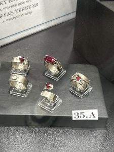 Five silver rings with red stones displayed in clear stands, labeled with "35.A" on a black surface.