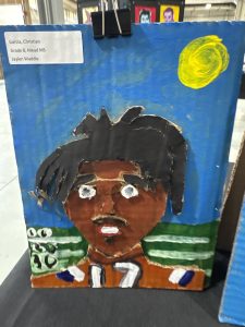 A colorful painting of a boy with dark hair and a brown face, wearing an orange shirt with the number 17.