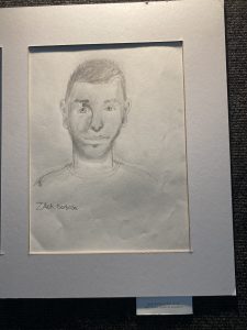 Pencil sketch of a young man with short hair, smiling, framed with a label indicating the artist's name and school.