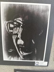 A monochrome digital charcoal portrait of a person with glasses, showing a dramatic expression and textured background.
