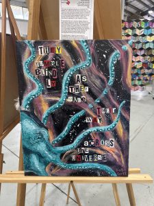 A colorful painting featuring an octopus with text that reads about tumbling across the universe, displayed on an easel.