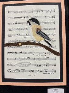 A painted bird sits on a branch, overlaying a background of sheet music. The artwork combines nature and music.