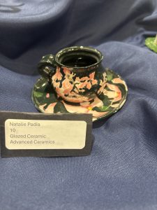 A small, floral-patterned ceramic cup and saucer displayed on a blue fabric background.