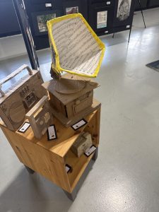 A wooden display holds cardboard models of a gramophone and a radio, with art pieces visible in the background.