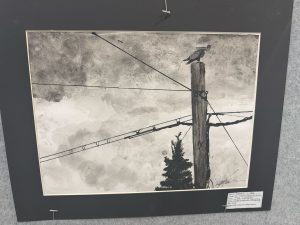 Black and white artwork depicting a utility pole with wires and a bird on top, set against a cloudy sky.