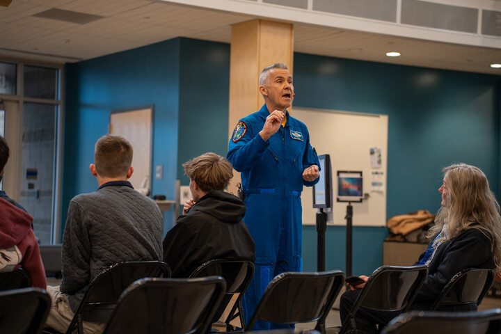 Duane Carey speaks to an audience seated in chairs in a modern indoor space.