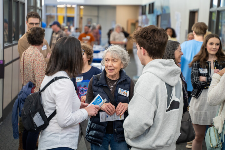 A group of people engage in conversation in a busy hallway during a community event.