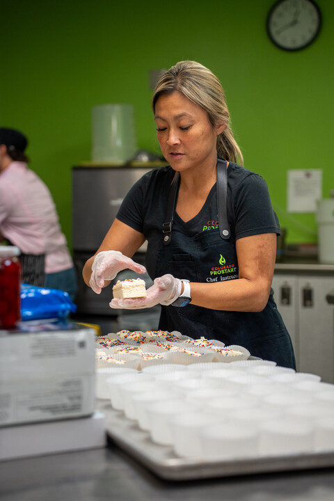 Una mujer, en la cocina, coloca un trozo de tarta glaseada y con virutas de colores en una bandeja donde ya hay más trozos de tarta.